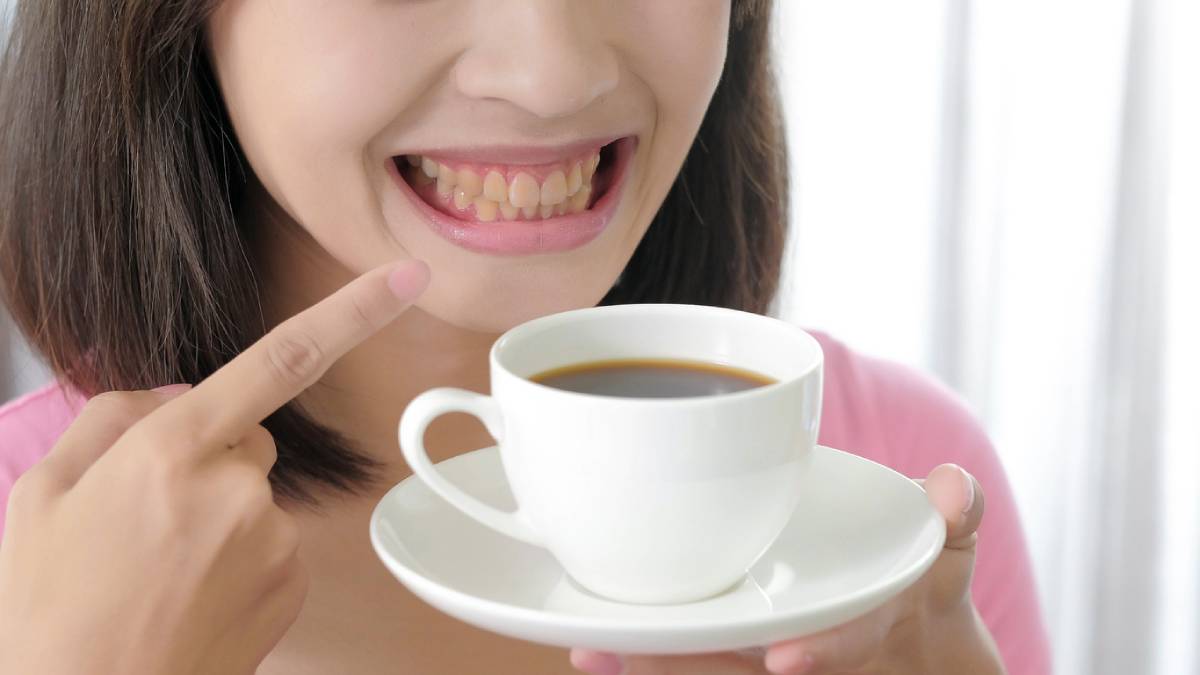 Woman with yellow teeth, pointing to coffee.