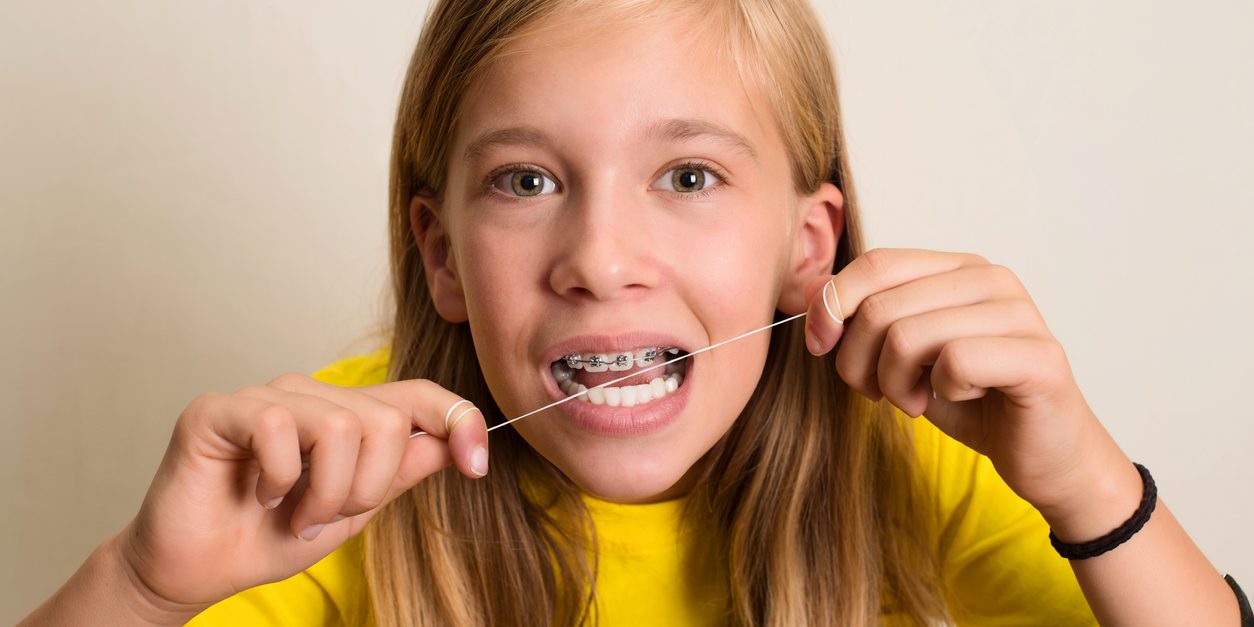 Young blonde girl with braces flossing.