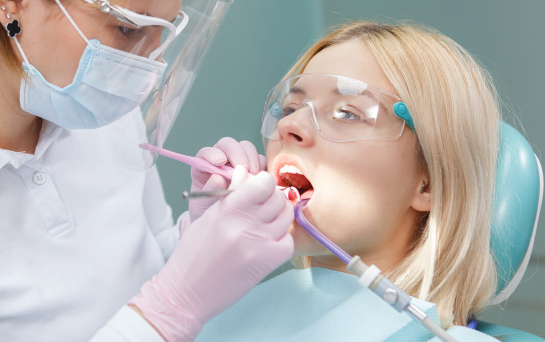 Young woman wearing protective glasses while dentist examining her teeth